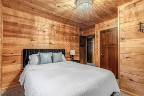 A wooden-paneled bedroom with a bed, a nightstand, a lamp, and a door. - Cozy Cottage on Turkey Lake/kayaks/Game room! (LaGrange)