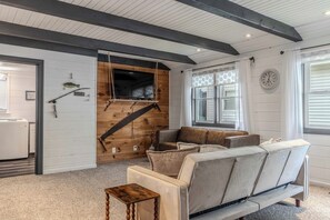 A cozy living room with a wooden wall, a television, a sofa, and a small table. - Cozy Cottage on Turkey Lake/kayaks/Game room! (LaGrange)