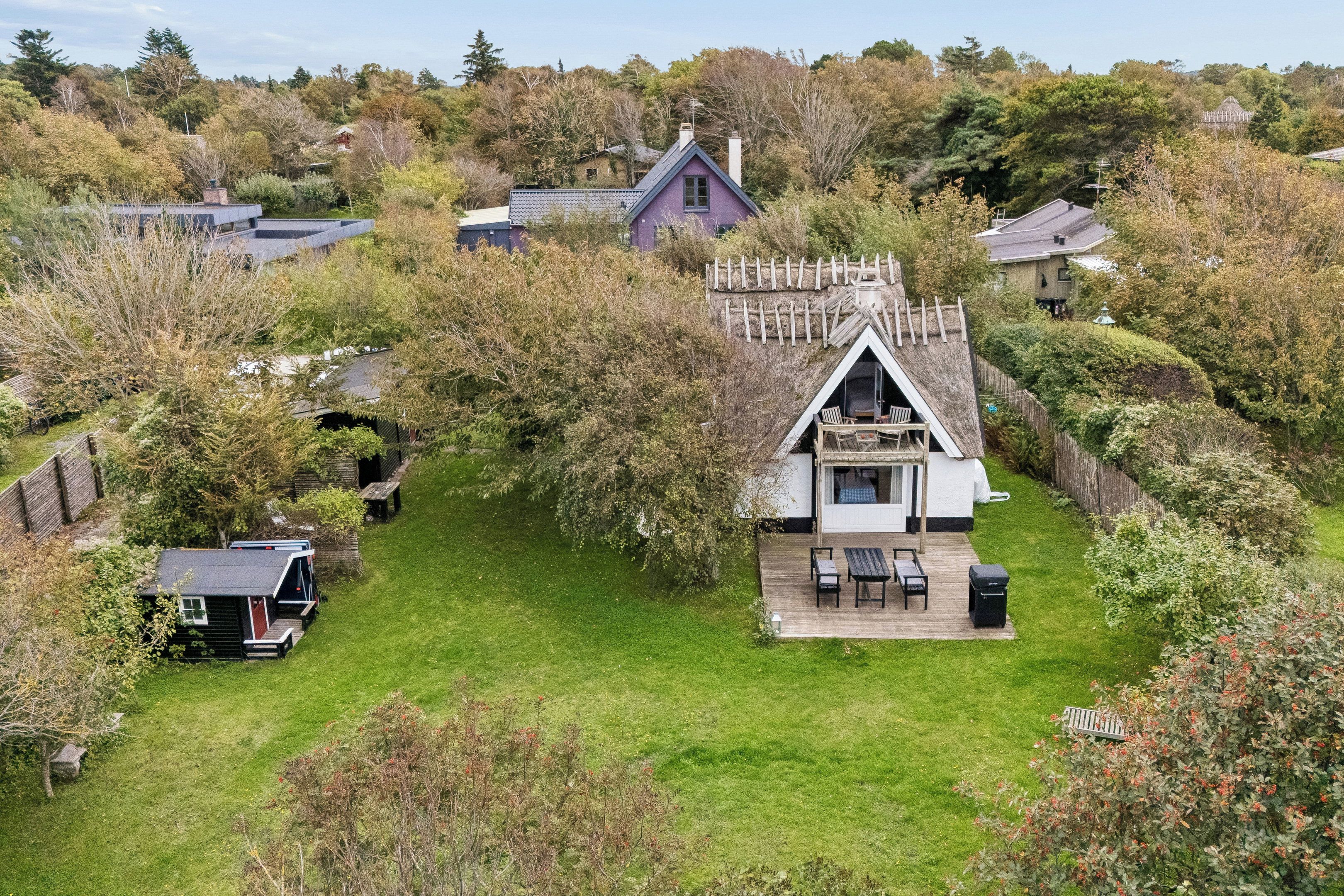 A house with a steeply pitched roof, surrounded by a well-maintained lawn and dense trees.
