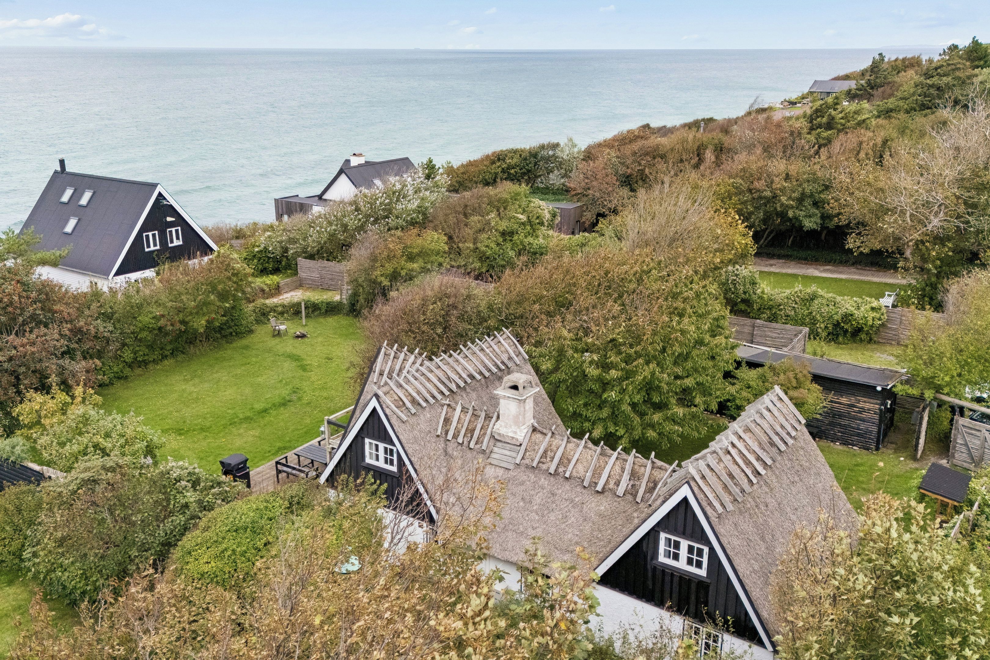 A coastal property with multiple houses, a grassy yard, and a view of the sea.