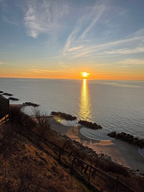 Ein Sonnenuntergang über einem ruhigen Meer mit einer felsigen Küstenlinie und einem Holzzaun.