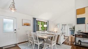 En matplats med ett träbord och vita stolar, ett fönster med gardiner och en hängande lampa.