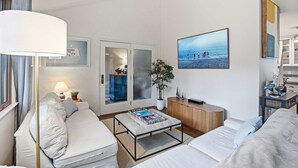 Ett modernt hotellrum med en soffa, ett soffbord, en bokhylla, en krukväxt och ett stort fönster med utsikt över stranden.