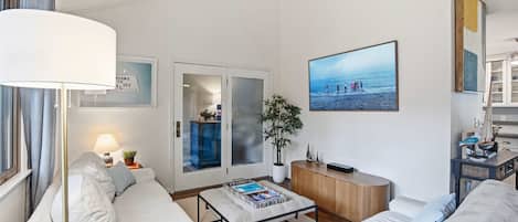 Et moderne hotelværelse med sofa, sofabord, reol, en potteplante og et stort vindue med havudsigt.