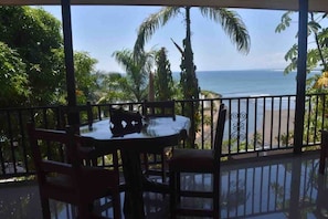 Een balkon met een tafel en stoelen, met uitzicht op een strand en palmbomen.