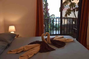 Een hotelkamer met een bed, een nachtkastje met een lamp en uitzicht op een balkon met planten.
