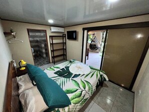 Ein Schlafzimmer mit einem Bett, einem Nachttisch mit Lampe, einem Hängesessel und einer Tür zu einem Badezimmer.