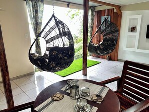 Uma sala de jantar com mesa redonda, cadeiras suspensas e vista para um gramado verde.