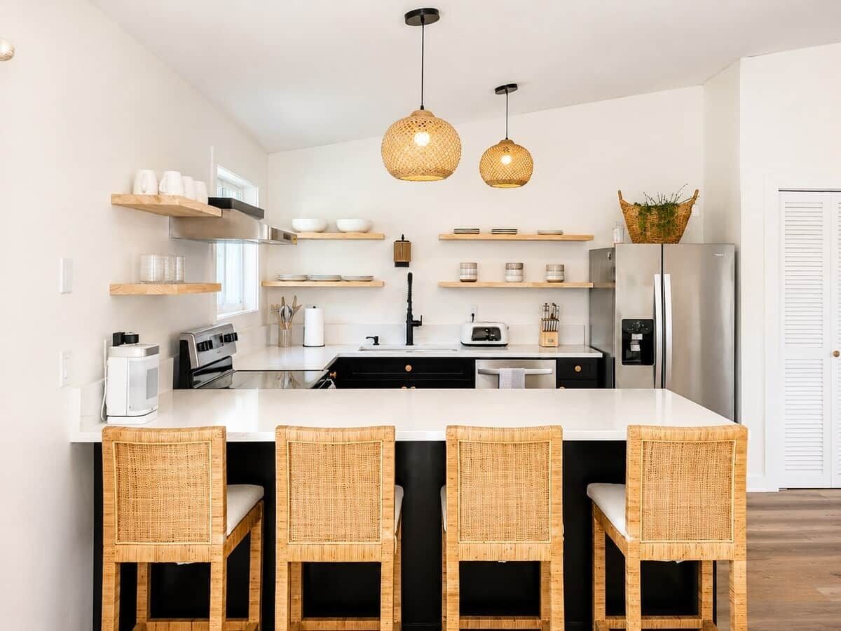 A modern kitchen with a central island, built-in appliances, and wicker chairs.