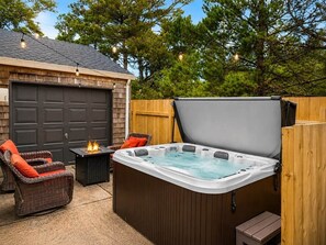 Ein Whirlpool mit Holzterrasse, ein Korbstuhl mit rotem Kissen und ein Tisch mit Feuerstelle.