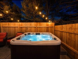A hot tub in an outdoor wooden enclosure with string lights.