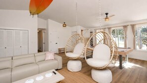 A modern living room with a sofa, two hanging chairs, a coffee table, and a ceiling fan.