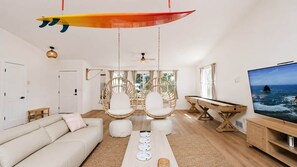 A modern living room with a sofa, two white chairs, a coffee table, a surfboard decoration, a TV, and a wooden table. - Sonny At The Coast (Cloverdale)