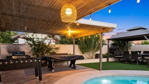 Area piscina all'aperto con barbecue, zona relax coperta e pergolato con luci a catena.