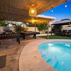 Ein Poolbereich im Freien mit Grillplatz, überdachter Sitzecke und einer Pergola mit Lichterketten.