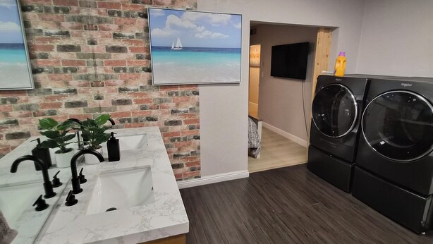 Un bagno moderno con un lavabo in marmo, rubinetti neri, un armadietto in legno, una parete decorata con mattoni e un quadro raffigurante una barca a vela. È presente anche una lavatrice.