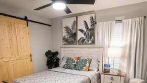 Una camera da letto con un letto di legno, un comodino, una ventola a soffitto e una finestra con tende.