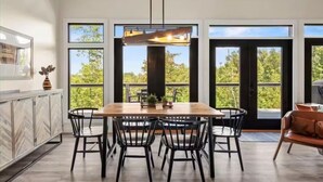Un espace repas avec une table et des chaises en bois, de grandes fenêtres et une vue sur la verdure.