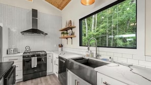 Une cuisine moderne dotée d’une grande fenêtre, d’appareils électroménagers en acier inoxydable et d’un dosseret en carreaux disposés en motif chevrons.