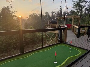 Eine Terrasse mit einem Minigolfplatz, einer Holzpergola und Blick auf den Sonnenuntergang.