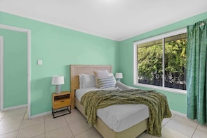 A bedroom with a bed, bedside tables, a window with curtains, and a view of greenery outside.