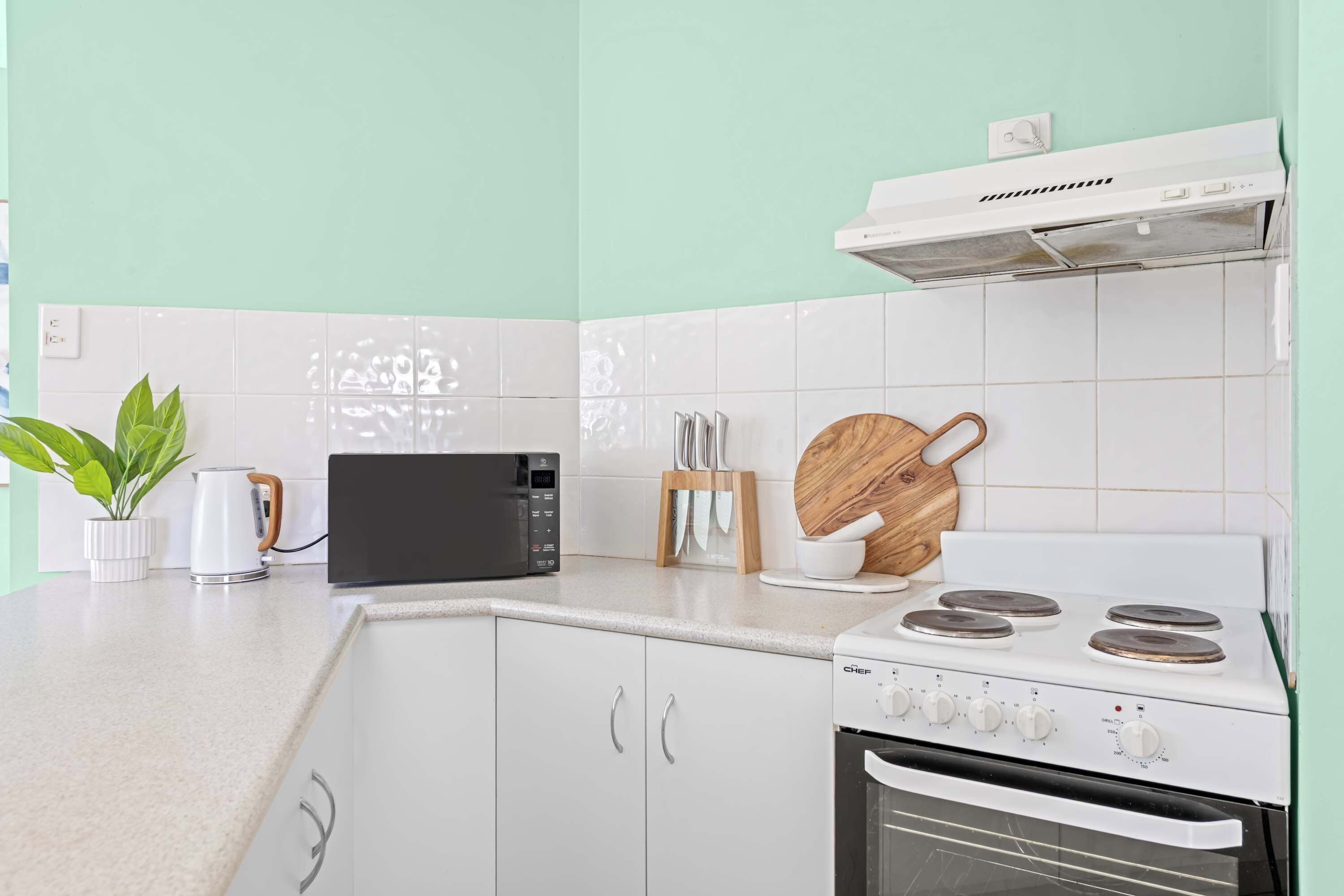 A modern kitchen with white cabinets, a black microwave, a white stove, and a wooden cutting board.