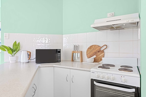 A modern kitchen with white cabinets, a black microwave, a white stove, and a wooden cutting board.