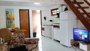 A spacious living area with a sofa, a dining table, and a kitchen with a refrigerator and a television. - Marina Guest House (Armação dos Búzios)