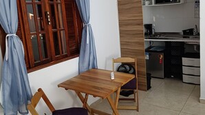 A compact living space with a dining area, a kitchenette, and a window with curtains. - Marina Guest House (Armação dos Búzios)