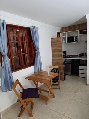 Ein kompakter Wohnbereich mit Essplatz, einer Küchenzeile und einem Fenster mit Vorhängen.