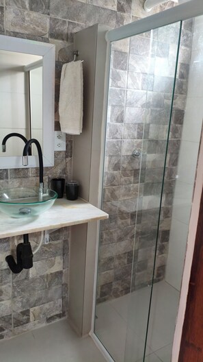 Ein Badezimmer mit Duschkabine aus Glas, einem Waschbecken mit Glasbecken und einem Handtuch an der Wand.