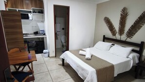 A hotel room with a bed, a desk, a chair, a microwave, and a bathroom. - Marina Guest House (Armação dos Búzios)