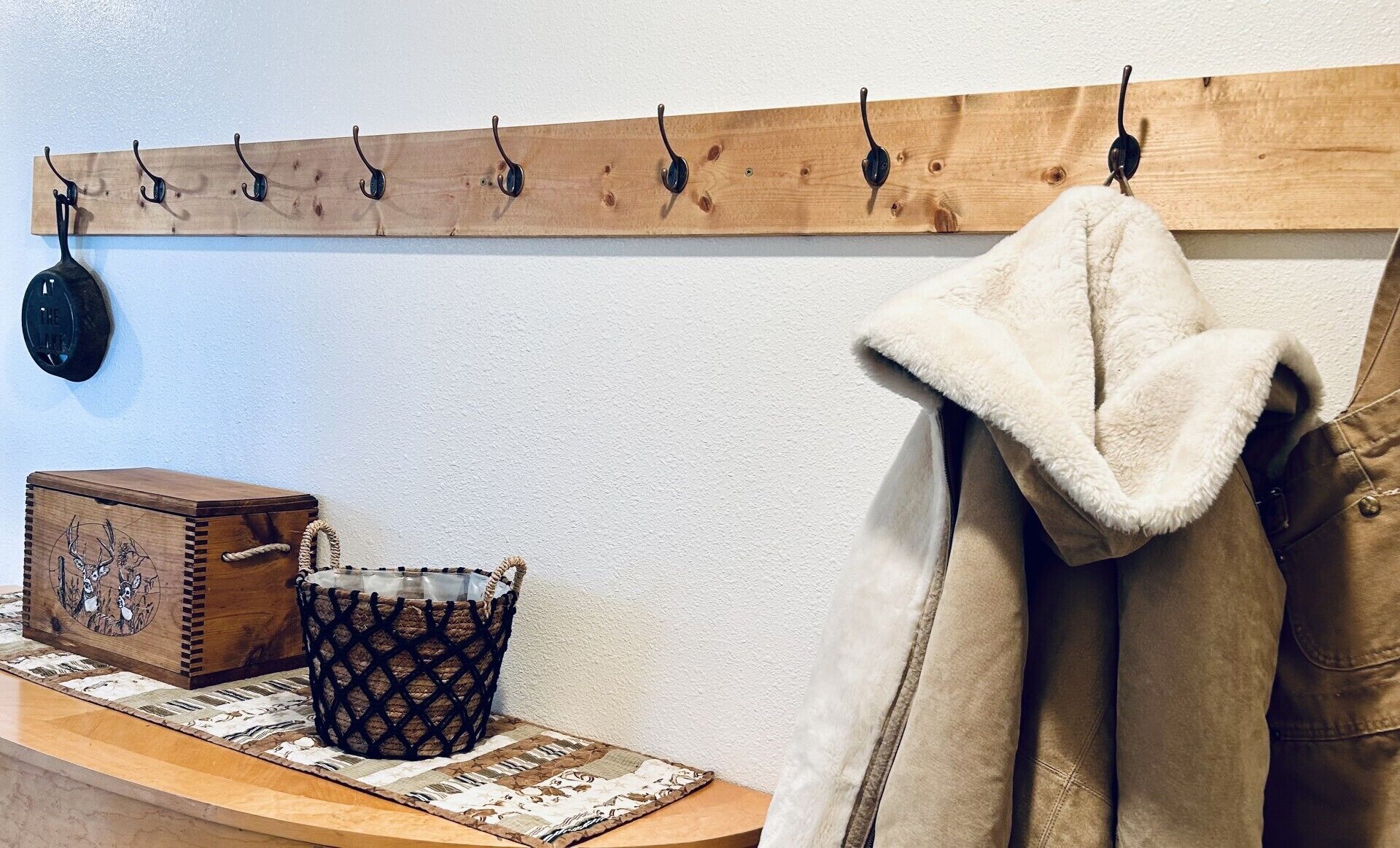 A wooden coat rack with hooks, a woven basket, a decorative box, and a fur-lined coat hanging on a wall.