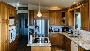 A kitchen with wooden cabinets, a stainless steel refrigerator, a built-in oven, a microwave, a coffee maker, and a sink. - Spectacular Home, Amazing Views, Outdoor Paradise (Lenore)