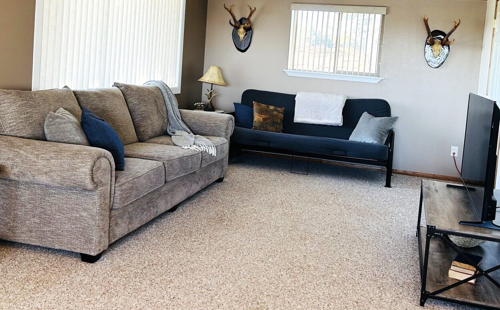 A living room with two sofas, a TV stand, and wall-mounted deer skulls.
