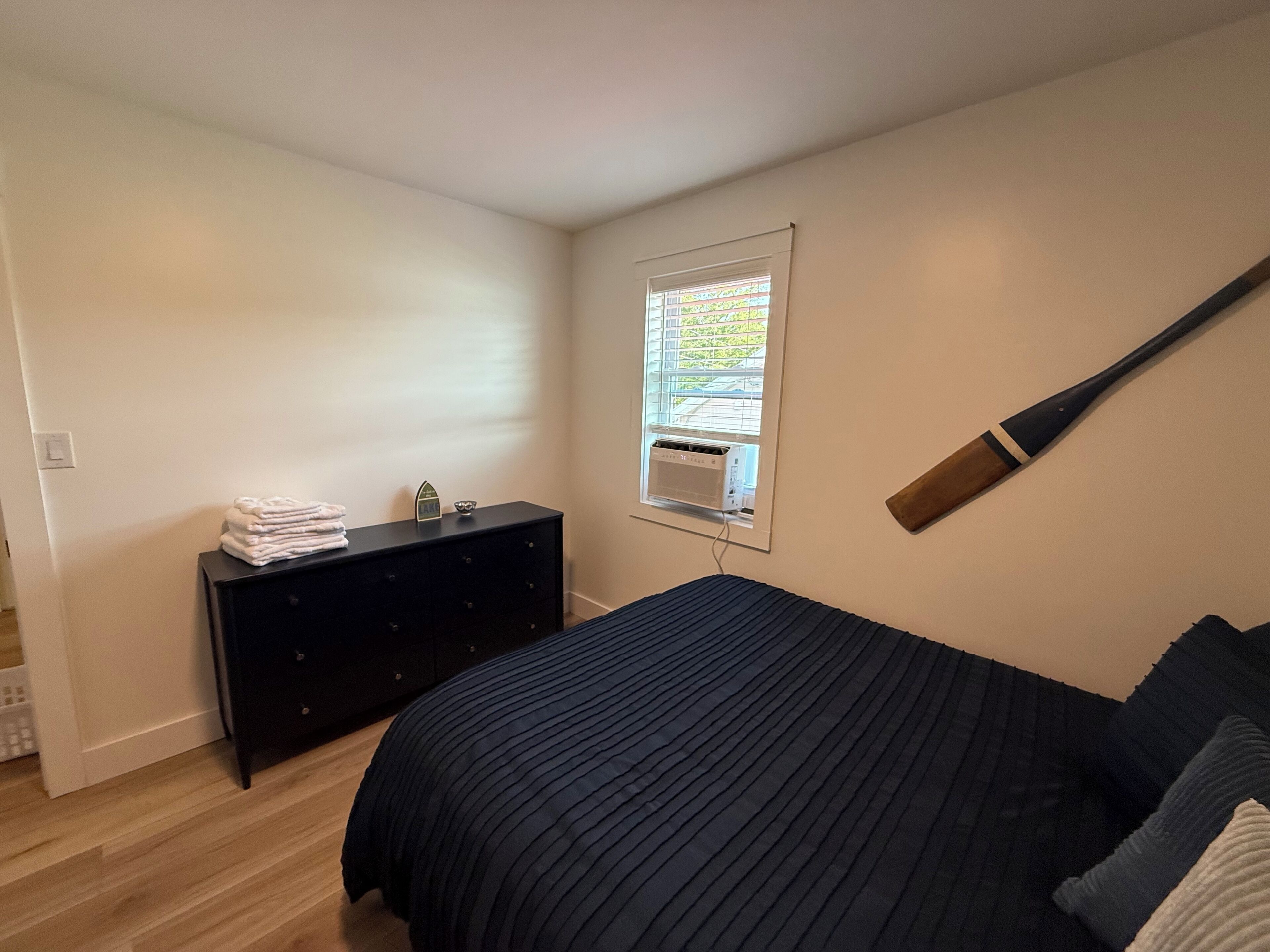 Um quarto com cama, cômoda, janela com persianas e um bastão de beisebol pendurado na parede.