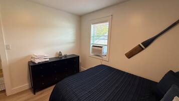Um quarto com cama, cômoda, janela com persianas e um bastão de beisebol pendurado na parede.