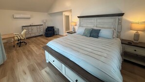 A bedroom with a large bed, a dresser, a desk, and an air conditioning unit. - Newly Renovated Family-Friendly 3-Bedroom Otisco Lake Home (Marietta)