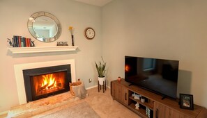 A living room with a fireplace, a television on a wooden stand, a clock, and a mirror on the wall. - Montview cottage  Walk to Burnet Rd, Central ATX (Austin)