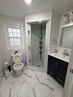 Un baño con inodoro, cabina de ducha, lavamanos y ventana.