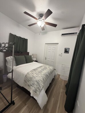 Un dormitorio con cama, ventilador de techo, equipo de aire acondicionado, una puerta y una ventana con cortinas.