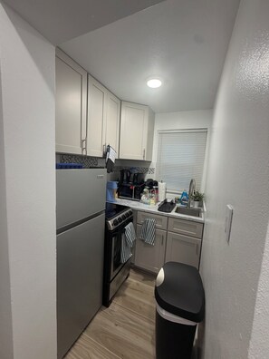 Cocina compacta con refrigerador, estufa, microondas y lavamanos.