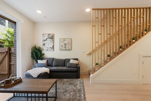 A modern living room with a grey sofa, a wooden coffee table, and a staircase with wooden railings. - Your Portland Chapter Starts Here, 2 Ensuites (Portland)