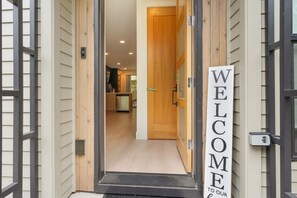 A doorway with a 'WELCOME TO OUR HOME' sign, leading into a modern kitchen with wooden cabinets and a stainless steel refrigerator. - Your Portland Chapter Starts Here, 2 Ensuites (Portland)