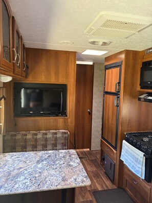 A compact RV kitchen with wooden cabinetry, a built-in microwave, a stove, and a television.