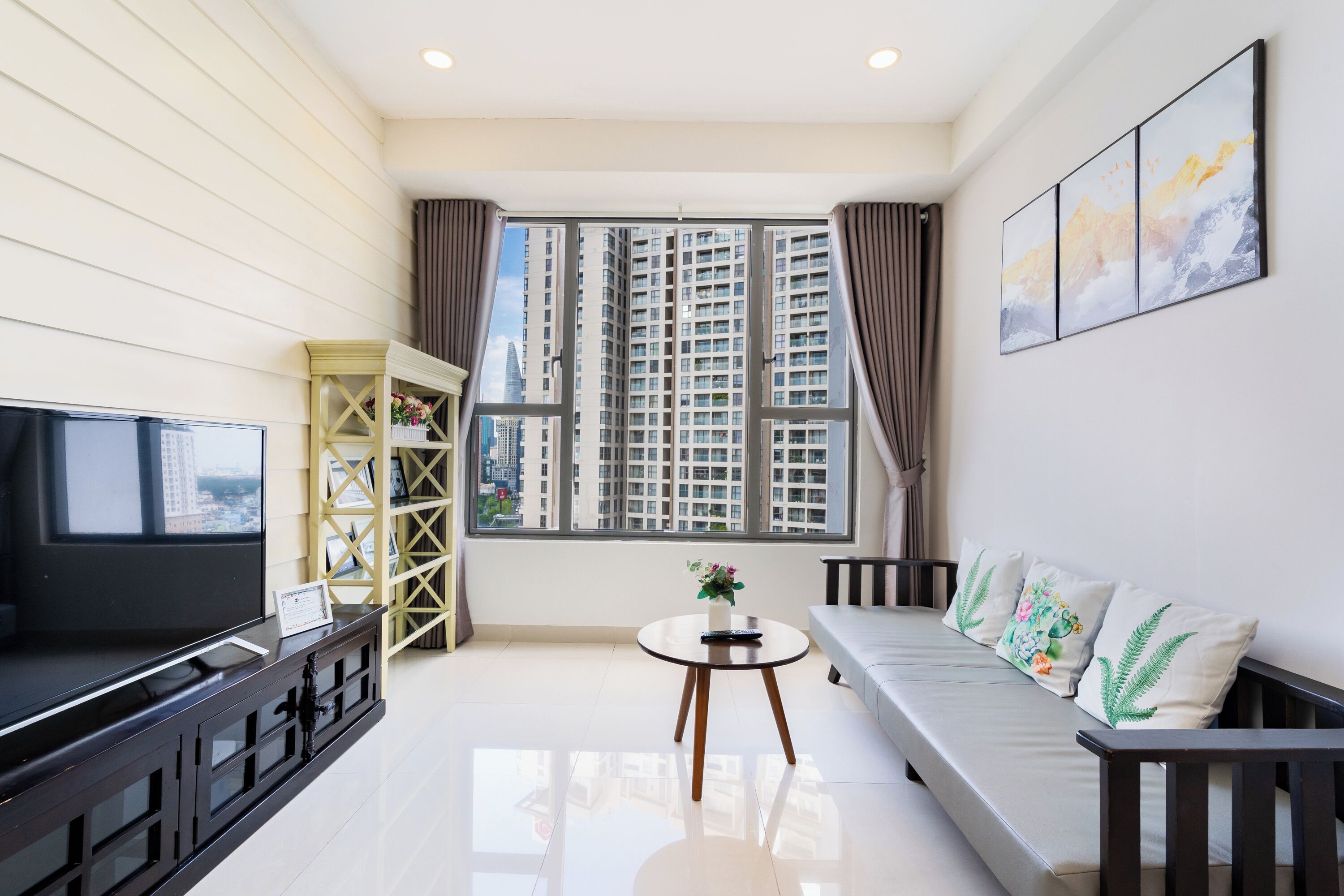 A modern living room with a flat-screen TV, a sofa, a coffee table, and a window with a city view.