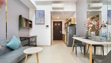 Uma sala de estar moderna com um sofá cinzento, uma mesa redonda pequena e uma cozinha com frigorífico e mesa de jantar.