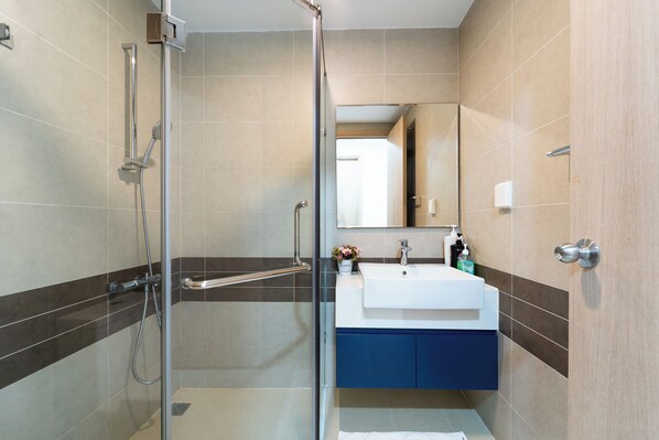 A modern bathroom with a glass shower enclosure, a white sink, and a blue cabinet.