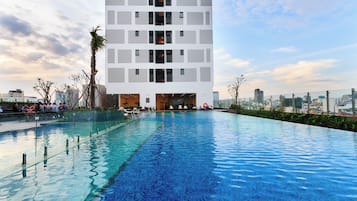 Um edifício moderno com piscina no terraço, rodeado por vegetação e uma paisagem urbana ao fundo.