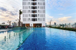A modern building with a rooftop pool, surrounded by greenery and a cityscape in the background. - GobyHome - Rivergate Residence Infi Pool (Ho Chi Minh City)